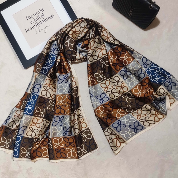 Luxurious women's scarf in brown and blue, beautifully draped next to a black bag and decorative frame.