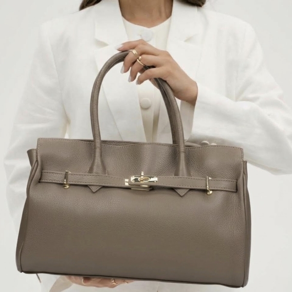 A model featuring a luxurious taupe-beige women's handbag made of genuine leather with gold accents.