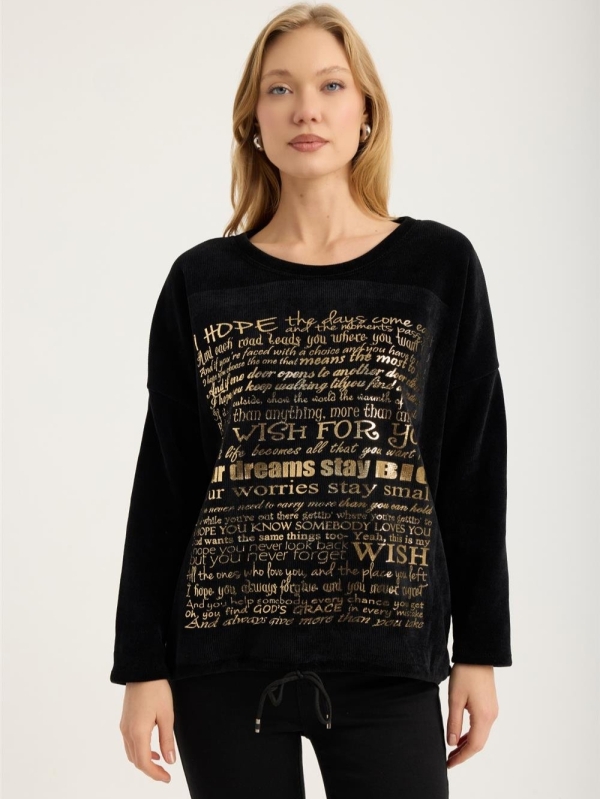 Blonde woman wearing a black ribbed blouse with gold lettering "My Wish For" and jeans"