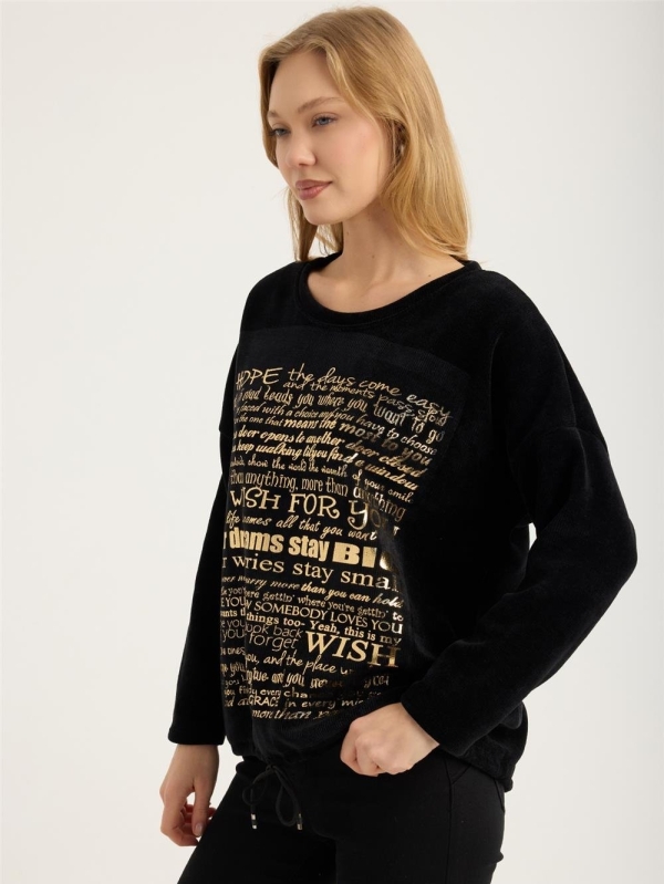 Blonde woman wearing a black ribbed blouse with gold lettering "My Wish For" and jeans"