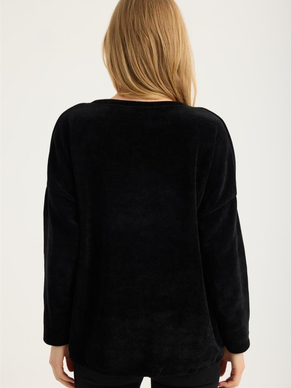 Blonde woman wearing a black ribbed blouse with gold lettering "My Wish For" and jeans"