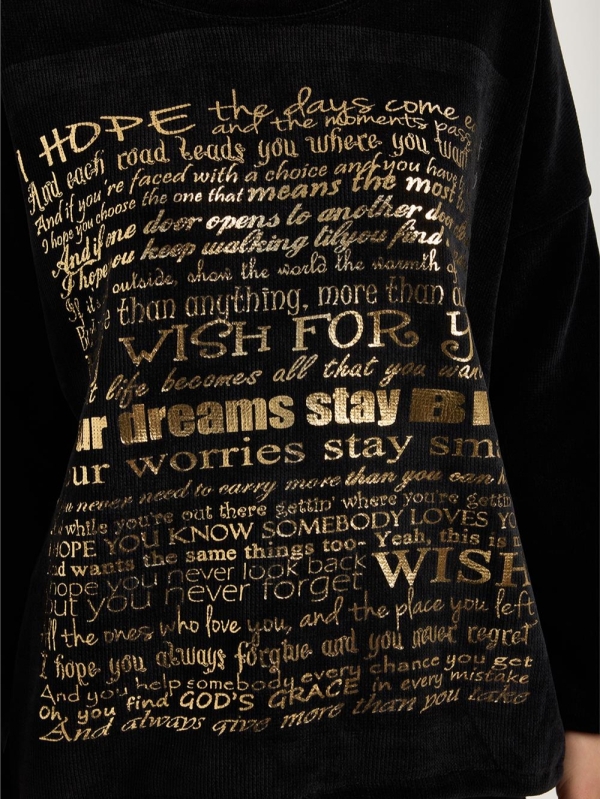 Blonde woman wearing a black ribbed blouse with gold lettering "My Wish For" and jeans"