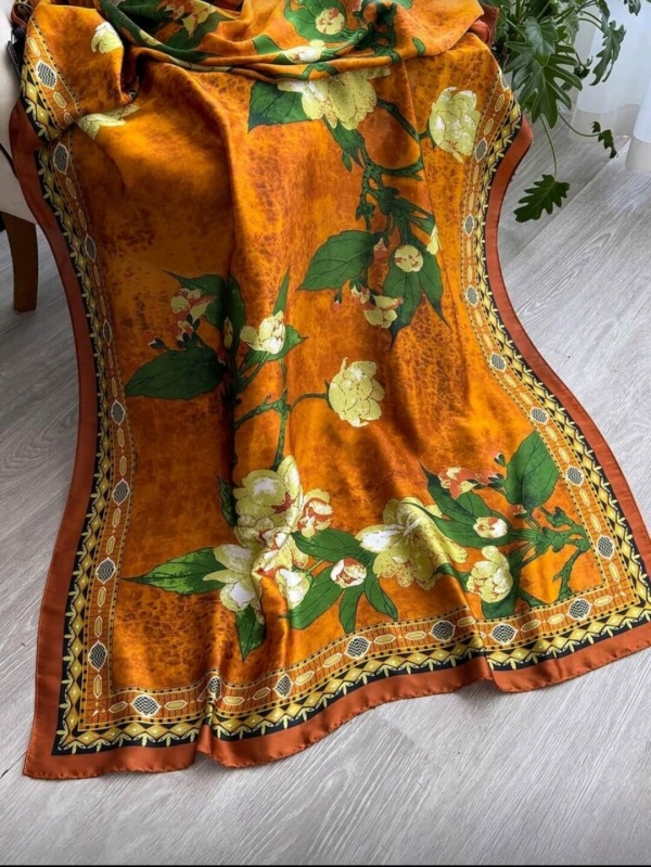 Long women's scarf made of polyester in orange with a print of yellow flowers and green leaves, casually draped