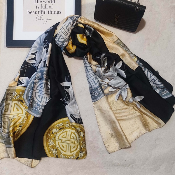 Елегантен дамски шал от коприна и вискоза, стилно вързан до черна чанта, черно и златисто.