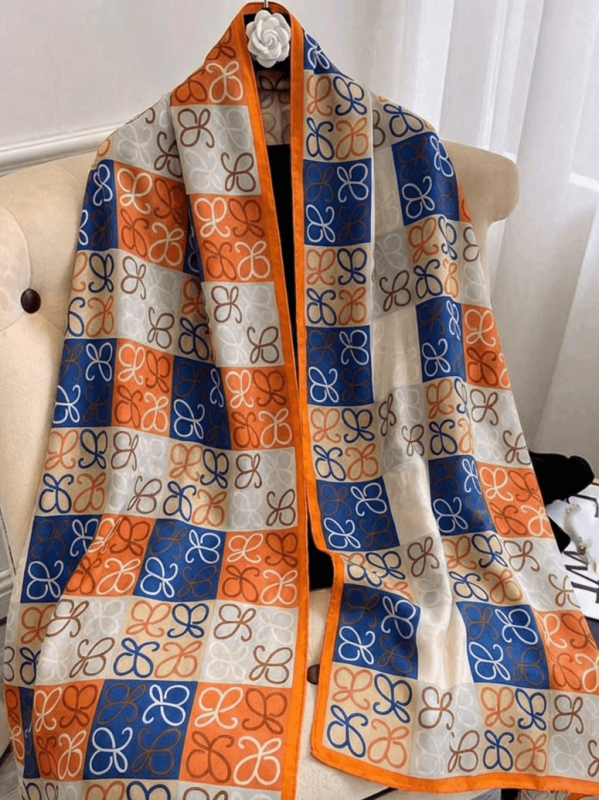 A large satin scarf with a geometric print in orange and blue, draped over a chair.