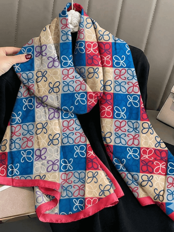 Women's satin scarf with a bright pink and blue geometric print, held in hand, showing off the softness of the fabric.
