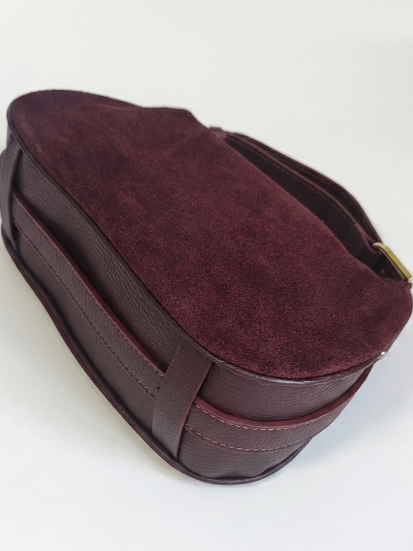 A detailed view of the bottom and sturdy leather structure of a women's suede bag in a rich burgundy color.