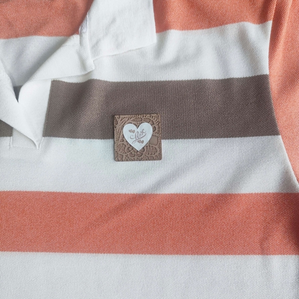 Близък план на декоративна емблема сърце с надпис Love върху дамска блуза на райе."