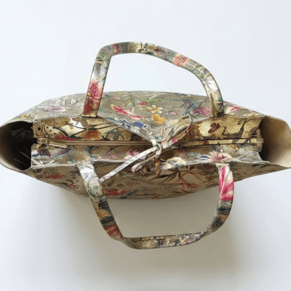 Поглед отгоре към италианска кожена чанта, показващ детайли на флоралния мотив, сигурното закопчаване с цип и деликатната декоративна кожена връзка.