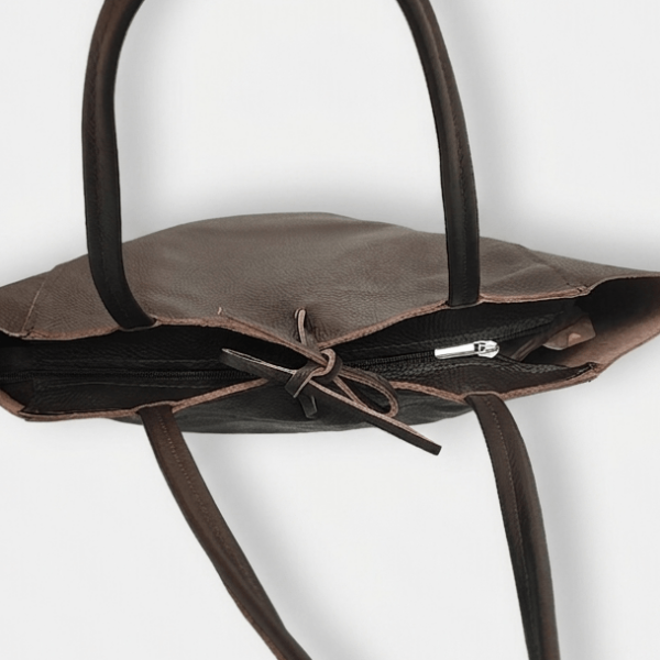 Detail of a secure zipper closure and leather ribbon on a large brown tote bag.