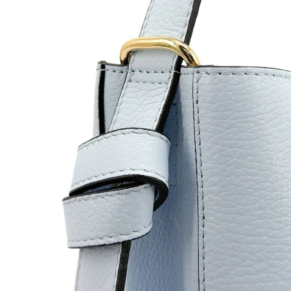 Close-up of a detail of a light blue women's leather bag, showing the attachment of the short handle with a gold buckle and black edges