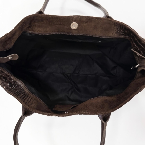 Top-down view of the interior of a dark brown bag with a black lining, a zipper, and a magnetic closure.