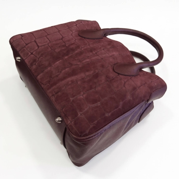 View of the bottom and the leather side panel of a burgundy Vera Pelle women's handbag.