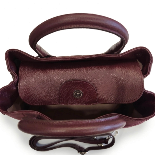 Detail of a closed leather flap with a magnetic snap on a burgundy women's handbag.